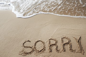 The word sorry writing on sand beach with waves ocean.