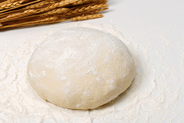 Raw fresh dough in the flour and ears of wheat on a white background