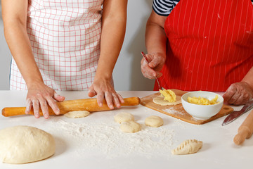 The family cooks together in the kitchen, close-up. Senior woman in a red kitchen apron sculpts cakes and adult daughter rolling dough with a rolling pin