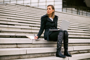 Beautiful businesswoman sitting on the staircase in the city and working.