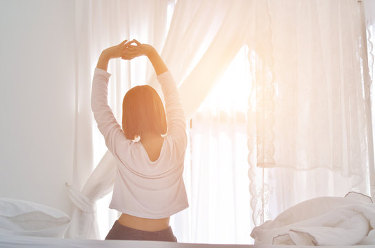 women sit at the edge of the bed. And stretching his arms to relax in the morning.Wake up in the morning.Warm tone.Do not focus on the object.