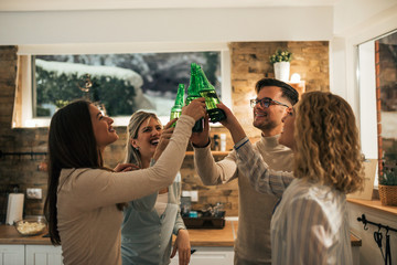 Best friends raised arms with bottles of beer celebrating at home in the evening.