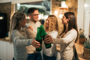 Friends clanging bottles of beer together. Focus on the foreground, on the bottles.