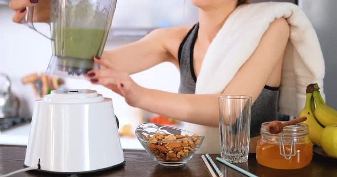 Young woman making green juice with juice machine in home kitchen after a workout.