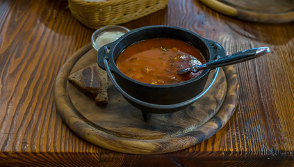 Russian soup, borsch, in a cast iron pot on the background of rye bread, on a wooden table in a stylish restaurant, in the old Russian style