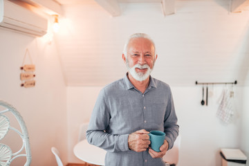 Portrait of a smiling senior man with a cup of coffee in a bright room, looking at camera.