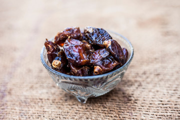 Close up of shot of raw organic dates or khajoor or Phoenix dactylifera in a glass bowl on a gunny bag background.