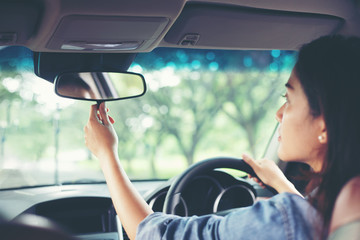 Asian women are adjusting the rearview mirror of the car