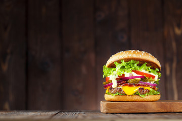 Delicious burger with bacon, cucumbers, lettuce, cheese, onion and tomatoes on dark wooden...