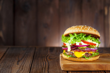 Delicious burger with bacon, cucumbers, lettuce, cheese, onion and tomatoes on dark wooden...