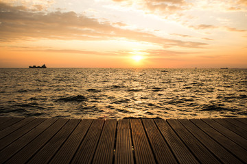 wooden deck waterfront shoreline and sea landscape horizon with ship in romantic sunset evening orange lighting time