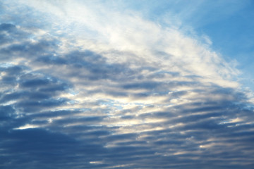 feathery clouds in the blue sky are illuminated by the rays of the sun, setting over the horizon