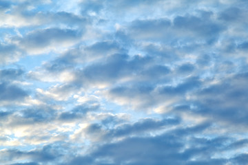 feathery clouds in the blue sky are illuminated by the rays of the sun, setting over the horizon