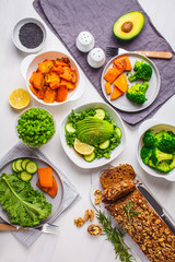 Healthy vegan food dinner table, top view. Green salad, sweet potato, vegan cake, vegetables on white background.