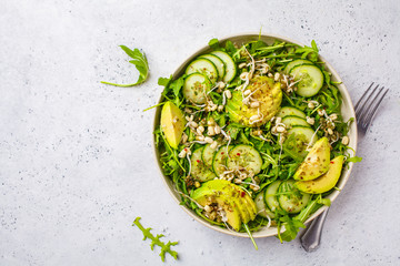 Healthy green salad with avocado, cucumber and arugula in white dish, top view, copy space.