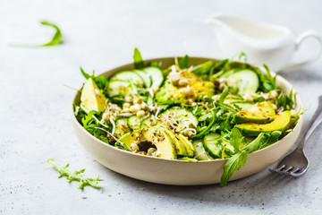Healthy green salad with avocado, cucumber and arugula in white dish.