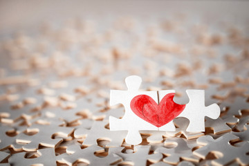 Two connected puzzle pieces containing two halfs of a red heart 