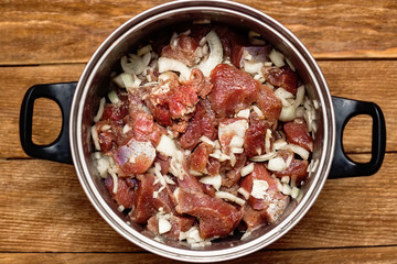 Marinated meat pieces with onions in pan on wooden background. Preparation of raw meat for barbecue. The view from the top. Raw beef mixed with onions and spices.
