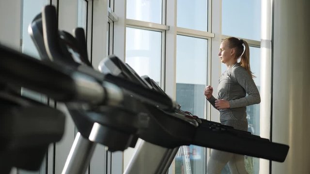 Attractive woman of middle age is running on tread mill in sport gym