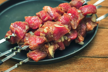 Raw fresh meat on skewers lies in a metal dish. Preparation of healthy food. Round tray with meat on wooden background. Close-up of food