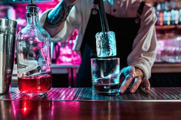 Expert barman is making cocktail at night club or bar. Glass of fiery cocktail on the bar counter against the background of bartenders hands with fire. Barman day concept