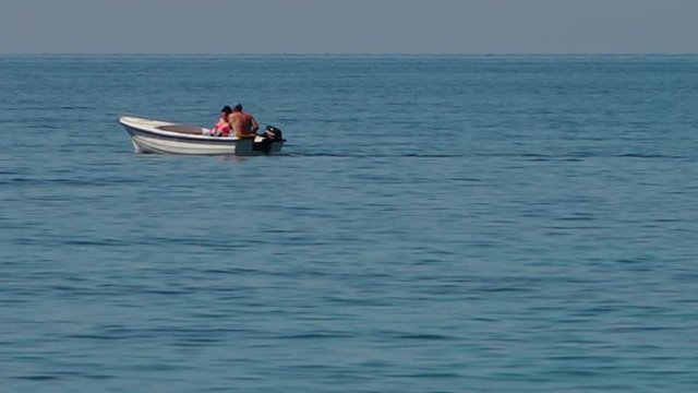 Mid shot of a small white boat with two people travelling across a calm ocean