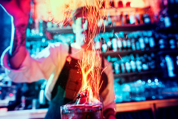 Glass of fiery cocktail on the bar counter against the background of bartenders hands with fire....