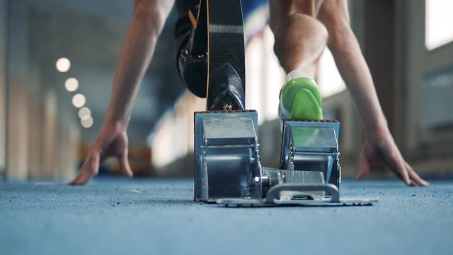 Man with bionic leg prosthesis starts to run on a track, back view.