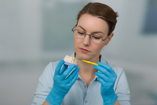 Zahntechnikerin bemalt einen Zahnersatz im Zahnlabor