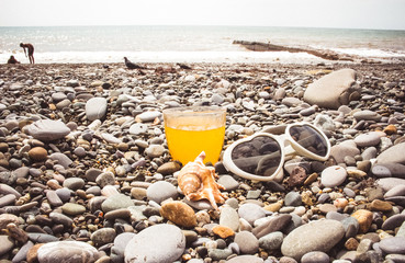 Fototapeta na wymiar A glass of juice, heart-shaped sunglasses and a large, beautiful seashell by the sea