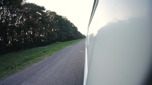 View of the car side with a 4k mounted camera opening views of the trees along the road and rolling down to the front wheel. Slow-motion.