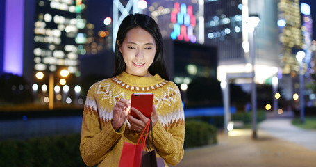 Woman look at mobile phone in city with shopping bag at night