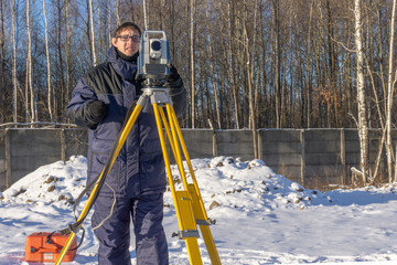 Surveyor conducts a topographical survey for the cadastre at a construction site in winter