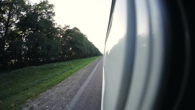 Camera attached on the side of the car rolling up and down opening views of the sky with clouds and trees passing-by when driving on highway in slow-motion. Close-up, wide angle.