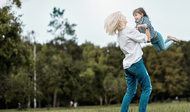Horizontal image of cute happy little girl playing with her beautiful mother in the park. Happy family time together. Positive emotion. Good relationship between mom and daughter. Mother's day concept