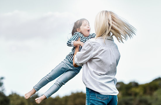 Outdoors image of happy little daughter playing with her smiling mother in the park. Loving woman and her little kid girl enjoying the time together. Mom and child has fun outside. Mother's day