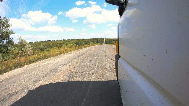 Camera attached on the side of the car when driving on rural road with trees passing-by on warm sunny day. Slow-motion.