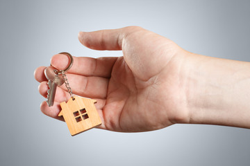 Hand of a real estate agent holding a house key on grey background