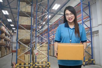 Pretty worker carrying box in the warehouse (ฺBlur background) ,Professional asian delivery woman bring the cardboard box in the distribution warehouse (ฺBlur background)