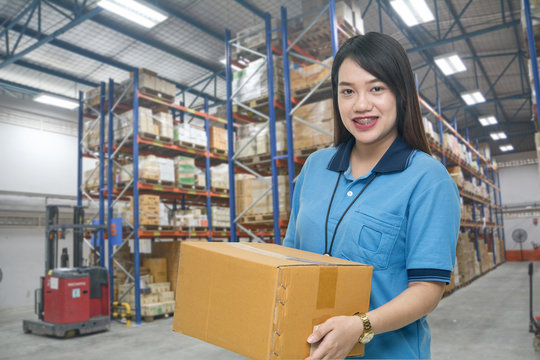 Pretty worker carrying box in the warehouse (ฺBlur background) ,Professional asian delivery woman bring the cardboard box in the distribution warehouse (ฺBlur background)