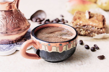 A cup of freshly brewed aromatic coffee next to a cezve and baklava on a light background