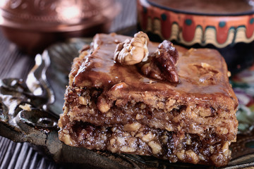 Baklava and cup of freshly brewed coffee next to a cezve on a wooden vintage tray and on a wooden background, macro
