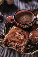 Baklava and cup of freshly brewed coffee next to a cezve on a wooden vintage tray and on a wooden background, vertical
