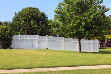 Fototapeta na wymiar White vinyl fence spanning across the back yard of a home with grass and trees