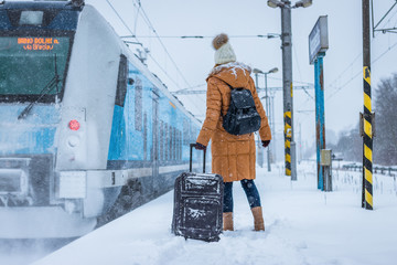 Woman with luggage is ready to board at arriving train on railroad station during snowing 