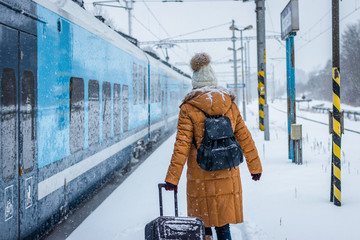 Woman with luggage is boarding to train on railroad station during snowing 