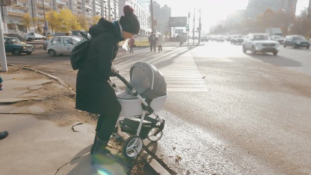 Slow motion shot of a woman struggling to push the pram from the pavement without ramp as she needs to cross the road