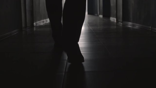 Dolly with low-section of silhouette of legs of man walking along hallway towards the camera