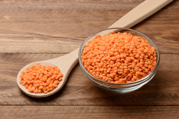 Lentejas naranjas crudas en un bol y una cuchara en la mesa de madera