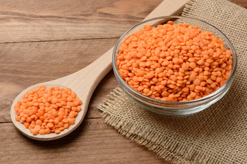 Lentejas naranjas crudas en un bol y una cuchara en la mesa de madera